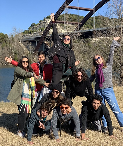 Group of students pose in a human body triangle on the shores of Lady Bird Lake