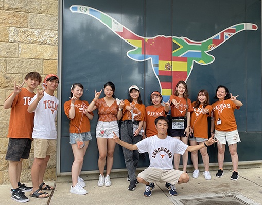 A group of students pose in front of the "Flag Bevo" painting made of international flags