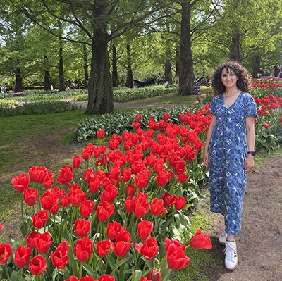 Jackie Villalobos, in a blue dress, stands beside a bed of red tulips