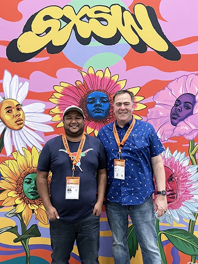 Ajmal and Gary stand in front of the SXSW 2023 selfie backdrop