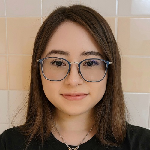 Student in a black top and glasses smiles at the camera