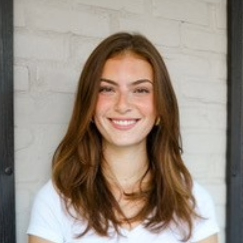Student in white top and medium-length brown hair smiles at camera