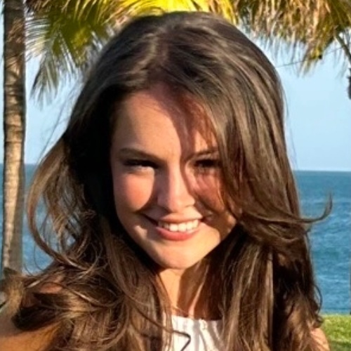 student with long brown hair smiles at camera in a tropical location