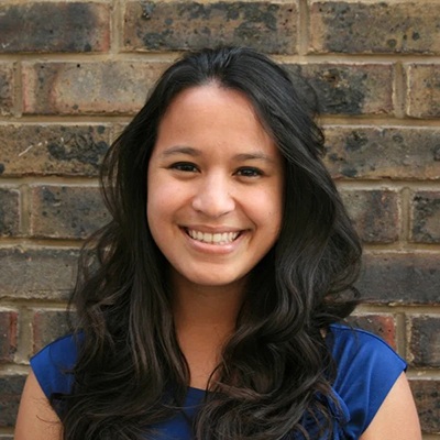 UT alumna Nadia Laabs smiles in a blue dress in front of a brick wall