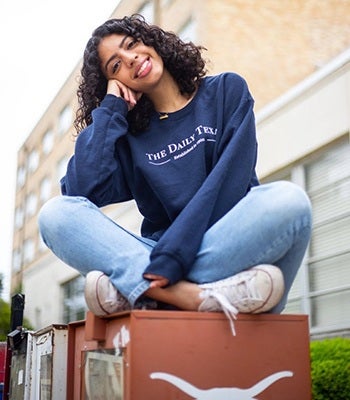 UT alum Leena Alali sits cross-legged atop a Daily Texan newspaper box