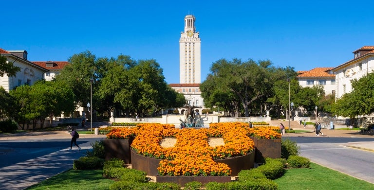 A view of the Tower at UT Austin with the logo in flowers and Littlefield fountain in view on a blue sky day