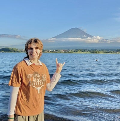Student puts up "hook em" hand sign in front of body of water.