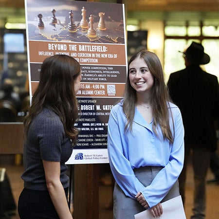 Two women stand beside the sign for the 2026 Texas National Security Forum