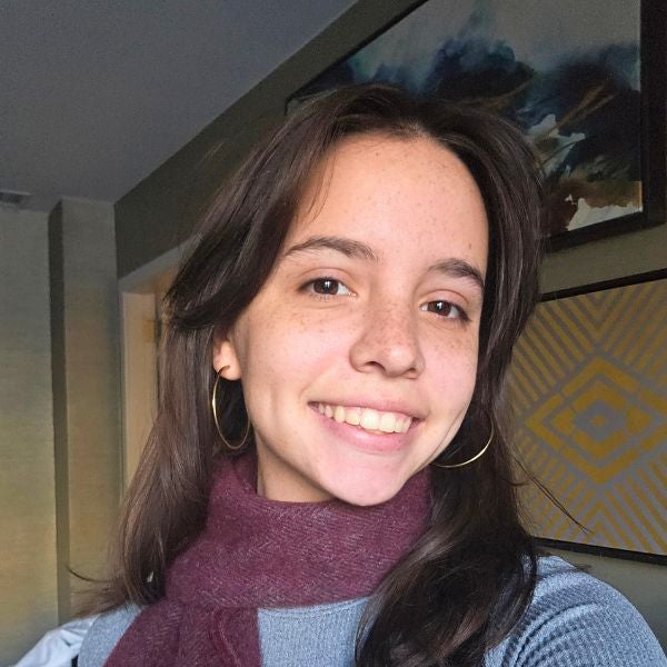 Person wearing a cozy maroon scarf and light blue sweater standing indoors with framed abstract art on the wall behind them.