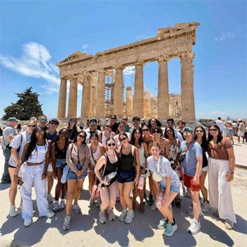 Students stand in front of Ancient Greek ruins.