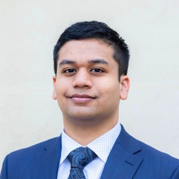 Young man in a blue suit and patterned tie posing against a plain light background.