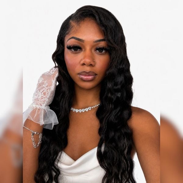Young woman with long wavy black hair wearing a white satin dress and delicate lace glove on one hand against a plain background.