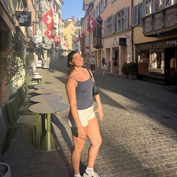 Young woman in casual summer clothes enjoying a sunny day on a cobblestone street lined with Swiss flags and outdoor café tables.