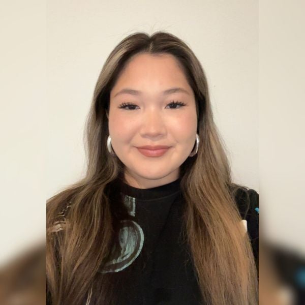 Young woman with long brown hair and hoop earrings smiling against a plain white background.